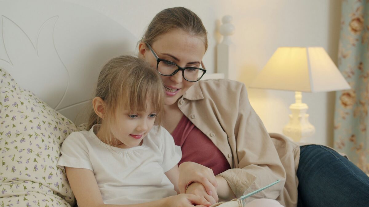 A mother and daughter smiling while reading a book together