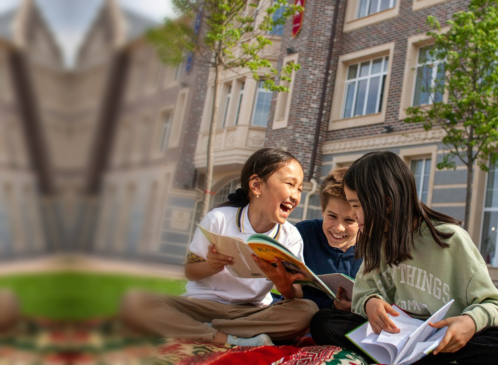 Three smiling children reading books together outside their school